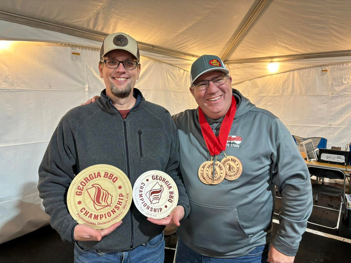 Two men standing inside a white tent, each holding a round wooden plaque.
